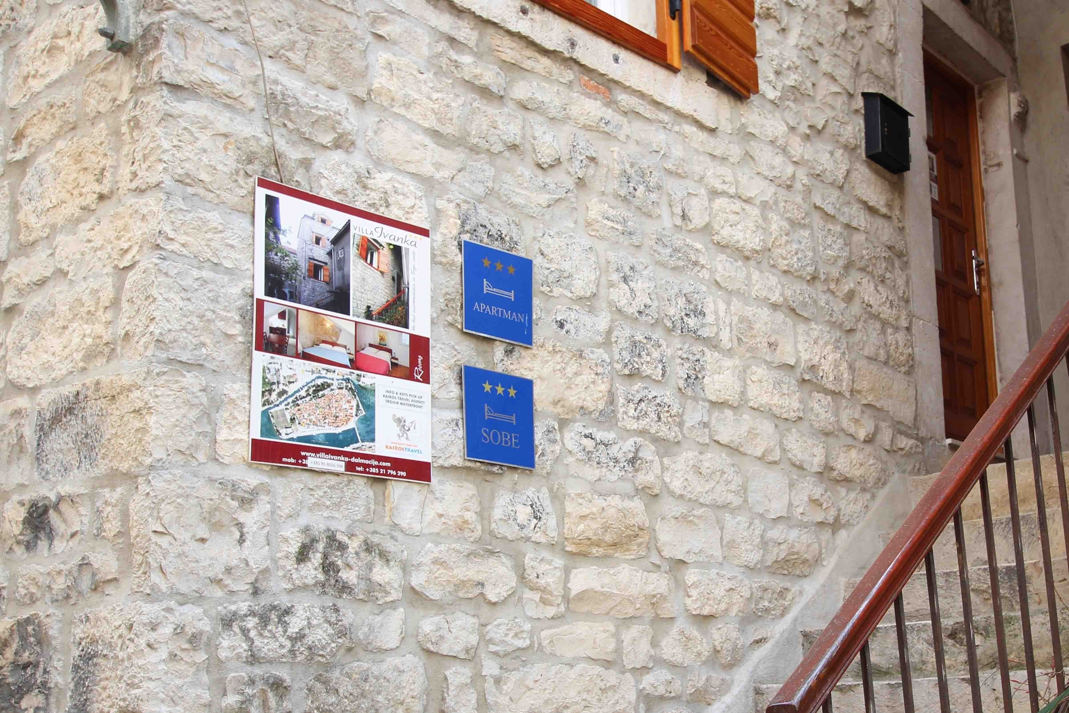 A stone building with a wooden staircase and two signs: one for 'Apartman' and another for 'Sobe'.