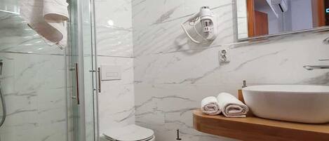 A modern bathroom with a glass shower enclosure, a white toilet, a wooden vanity with a sink, and a marble backsplash.