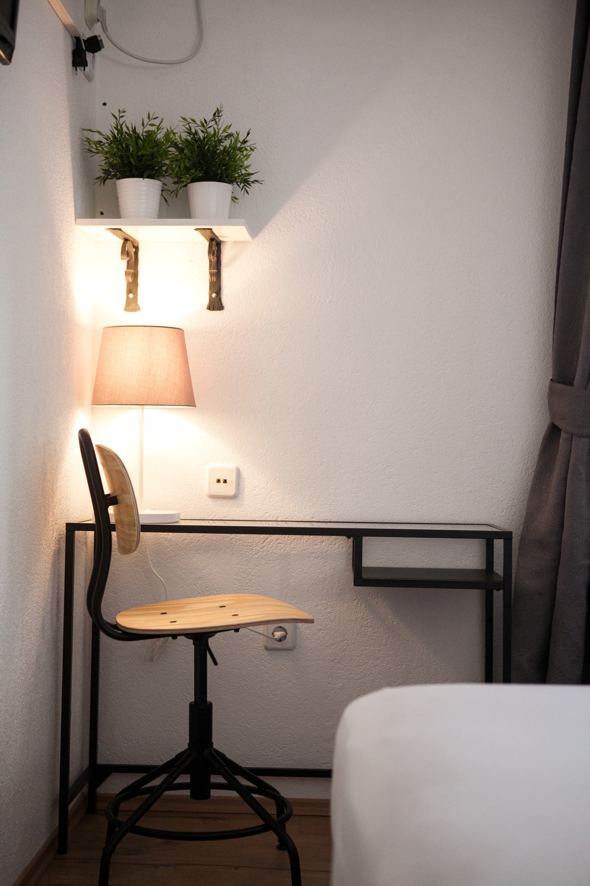 Un espacio de trabajo pequeño con escritorio, silla, lámpara y dos plantas en macetas.