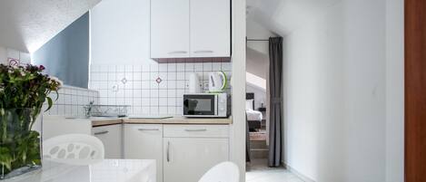 A modern kitchen with white cabinets, a microwave, and a sink. There is a dining table with chairs and a vase of flowers.