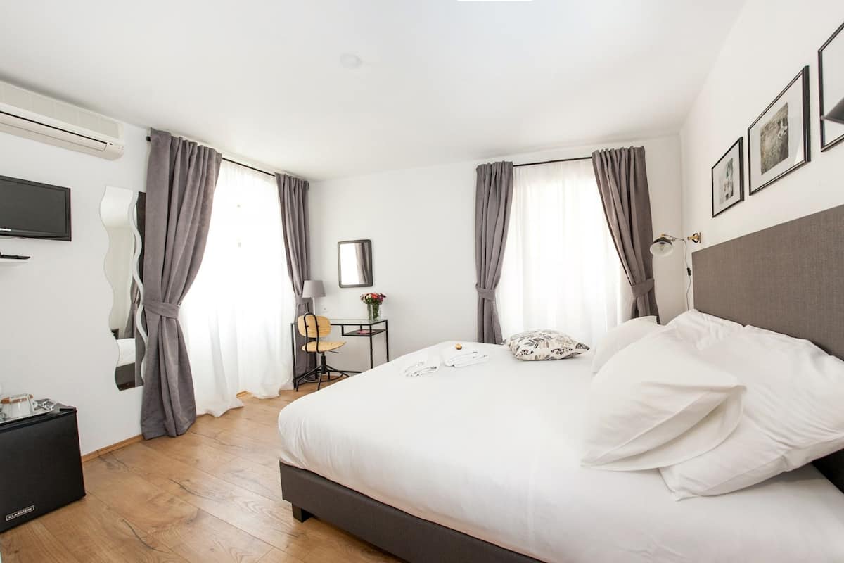 A hotel room with a bed, a desk, a chair, a TV, and a lamp.