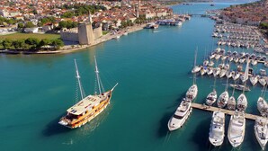 Un puerto deportivo con numerosas embarcaciones amarradas, una imponente construcción al estilo de castillo y un pueblo densamente poblado al fondo.
