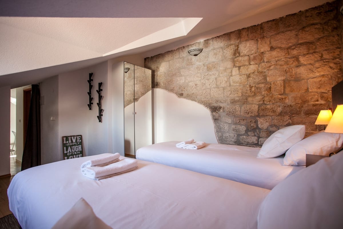 A hotel room with two beds, a stone wall, a mirror, and a sign that says "LIVE SIMPLY LAUGH OFTEN LOVE".