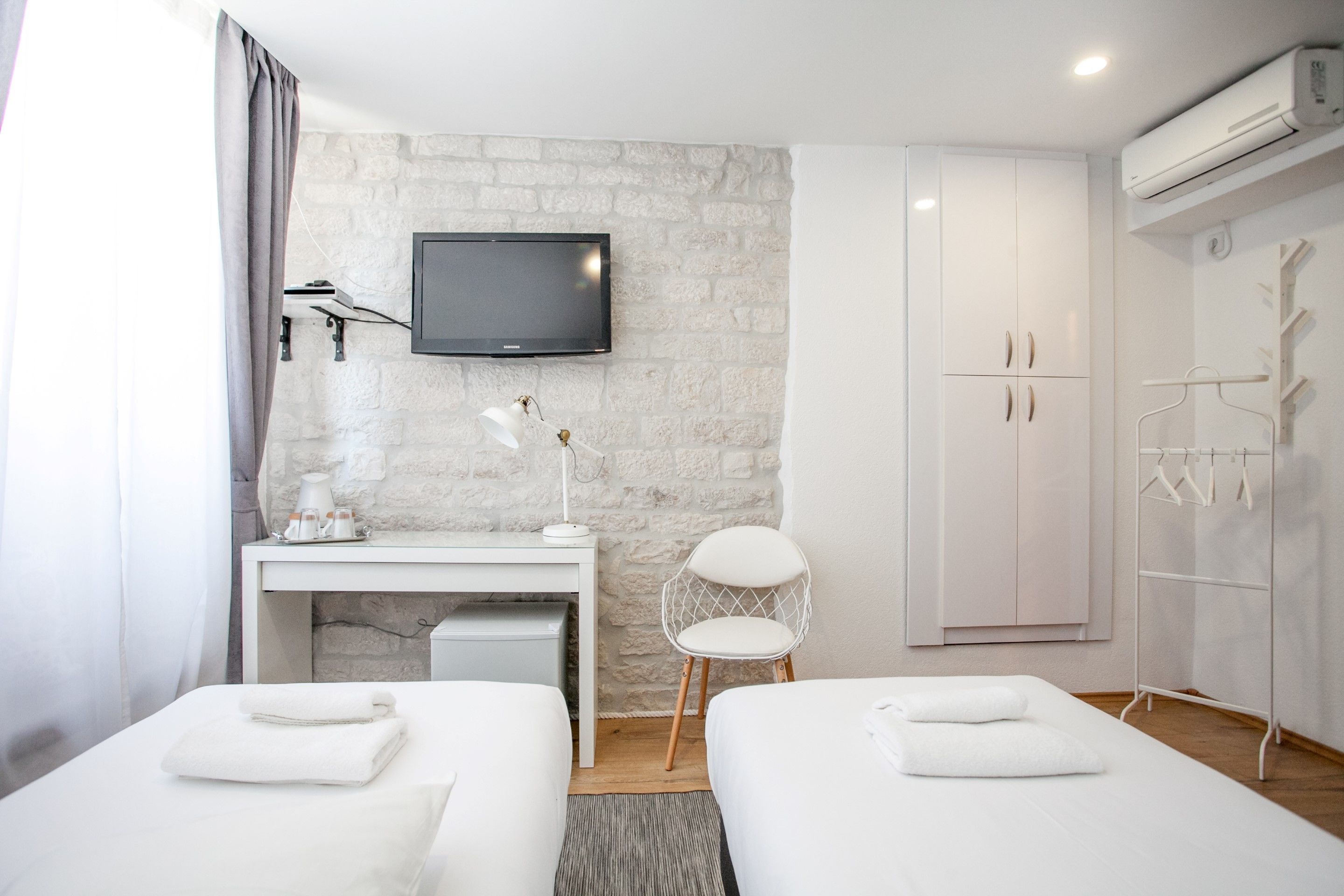 Habitación de hotel con dos camas, un escritorio, una silla, un televisor, un armario y un perchero.
