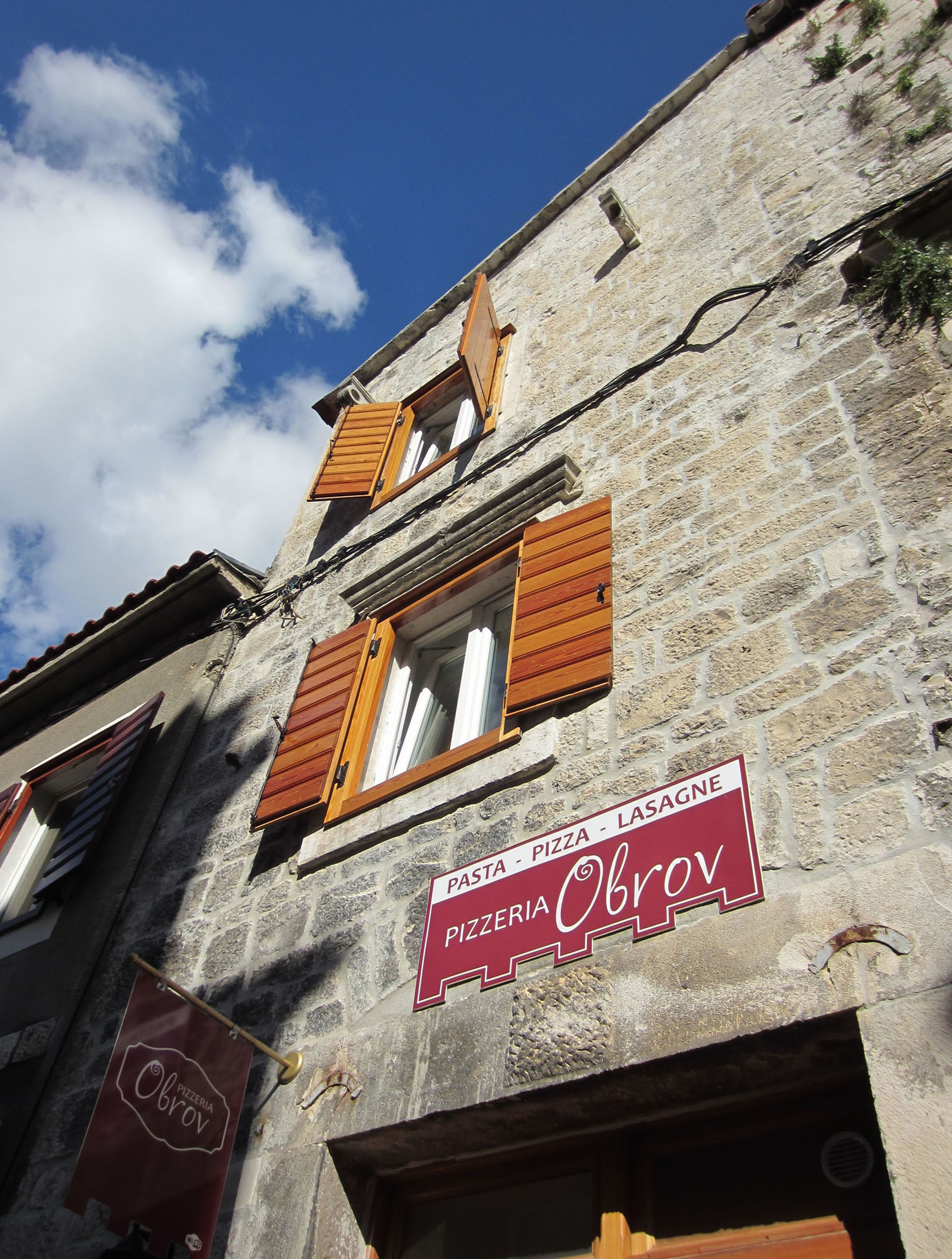 Un edificio de piedra con contraventanas de madera y un letrero que dice 'Pizzeria Obrov'.