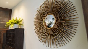 A wall-mounted mirror with a sunburst design, a dark wooden cabinet, and a potted plant. - Hotel Madrisol (Madrid)
