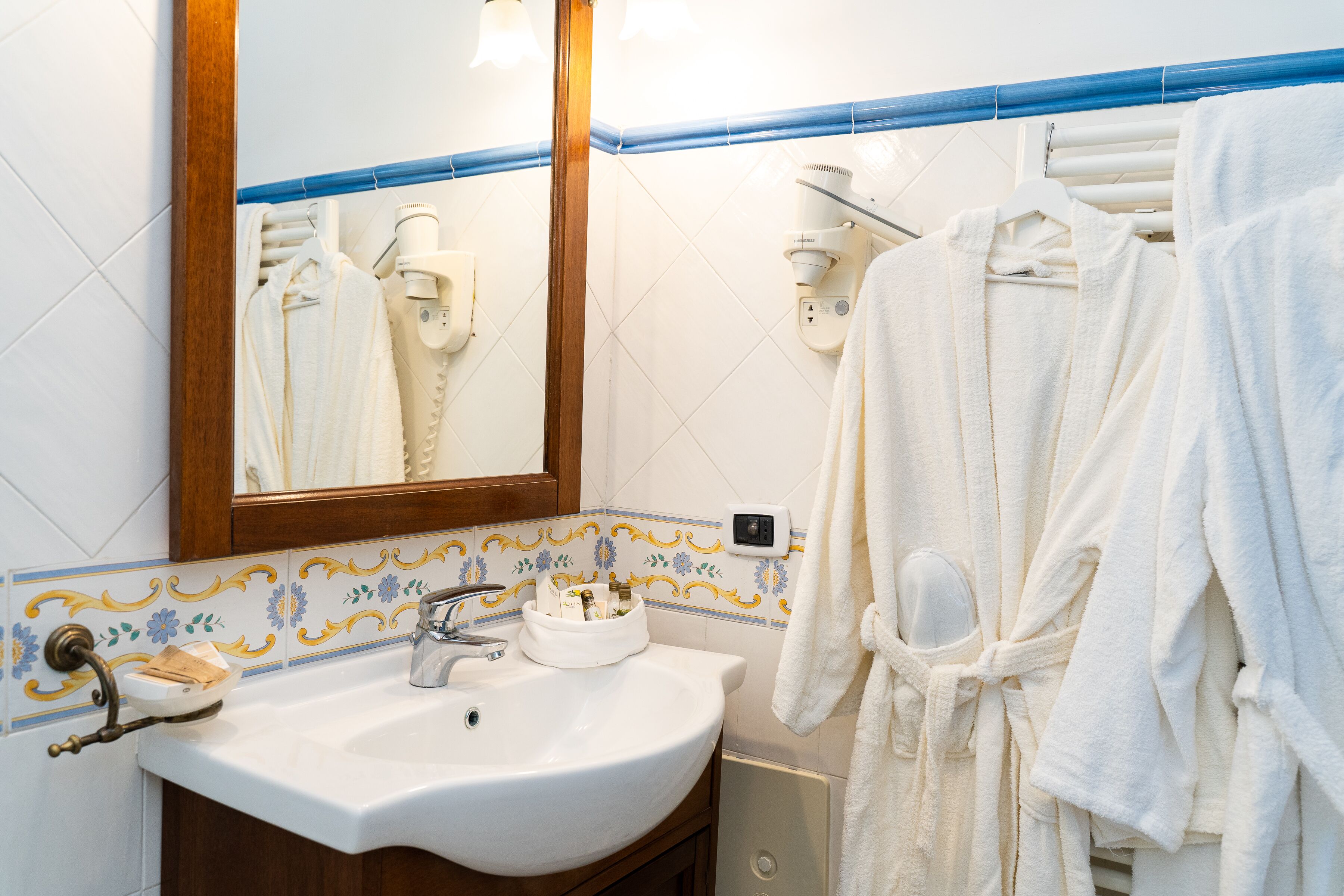 Une salle de bain avec un lavabo blanc, un miroir et un porte-serviettes sur lequel sont disposées des peignoirs blancs.