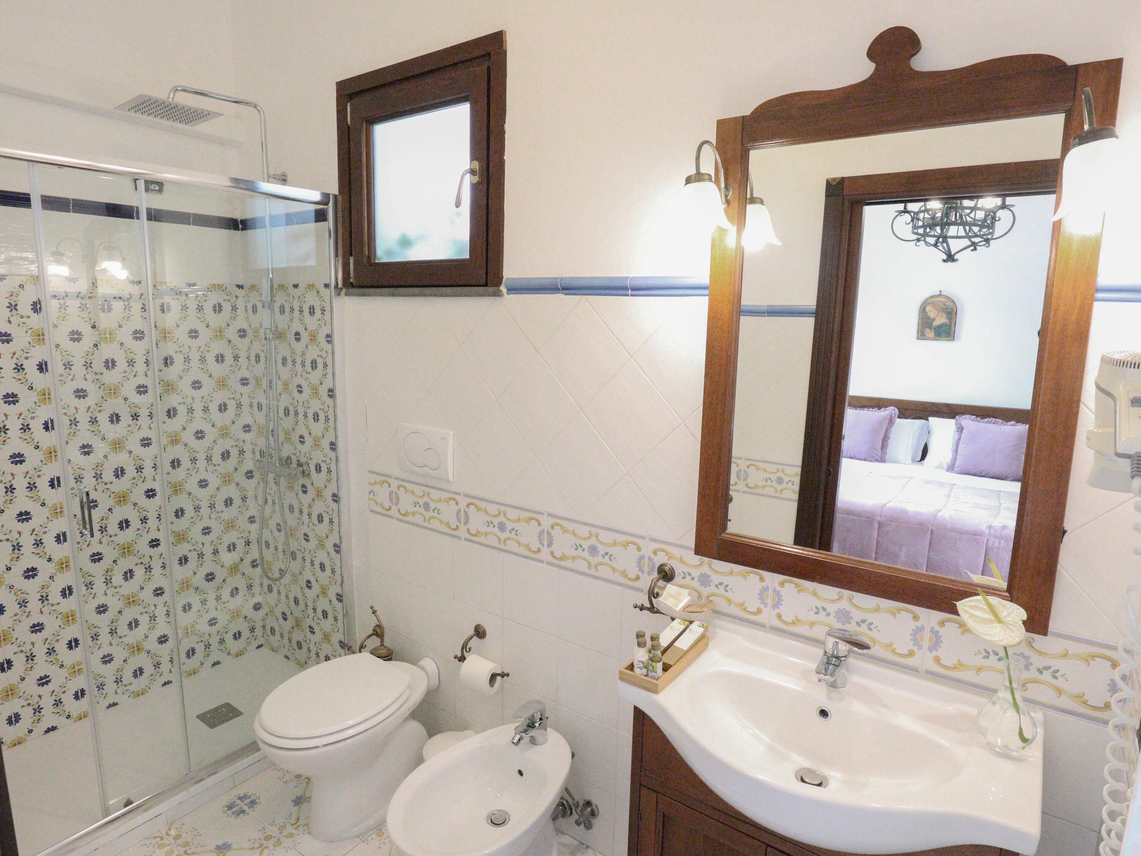 A bathroom with a toilet, bidet, and sink, featuring patterned tiles and a mirror.