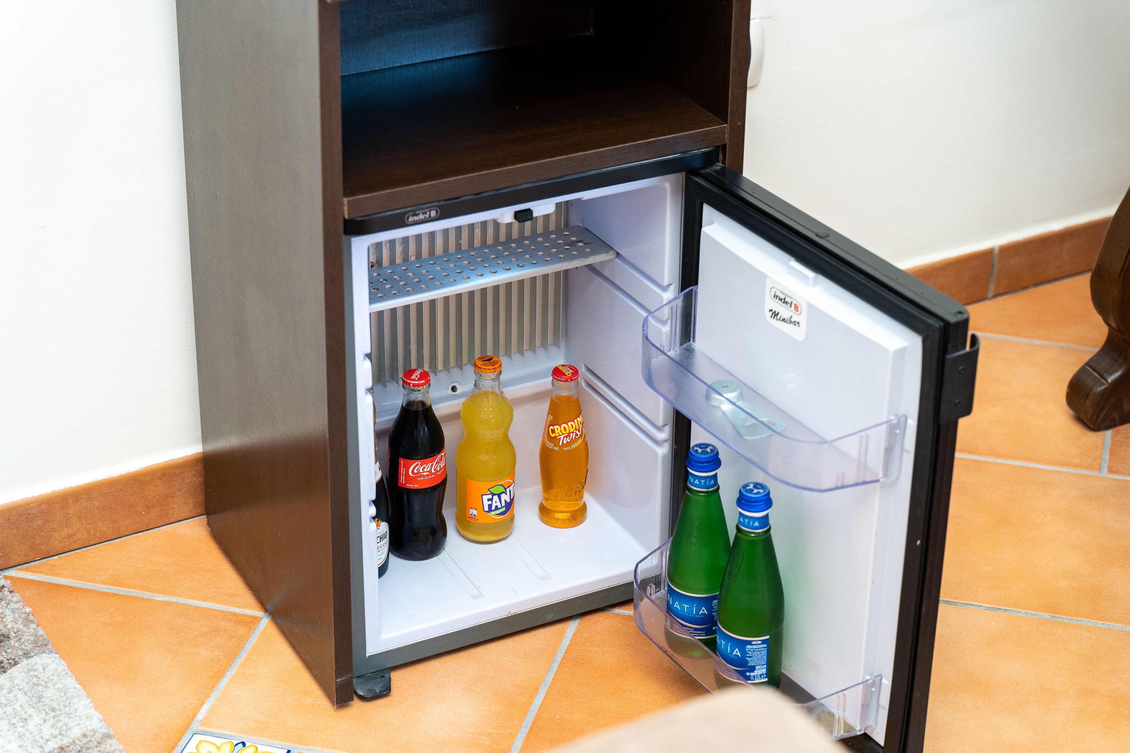 A small refrigerator with a shelf and a door shelf, containing various beverages.
