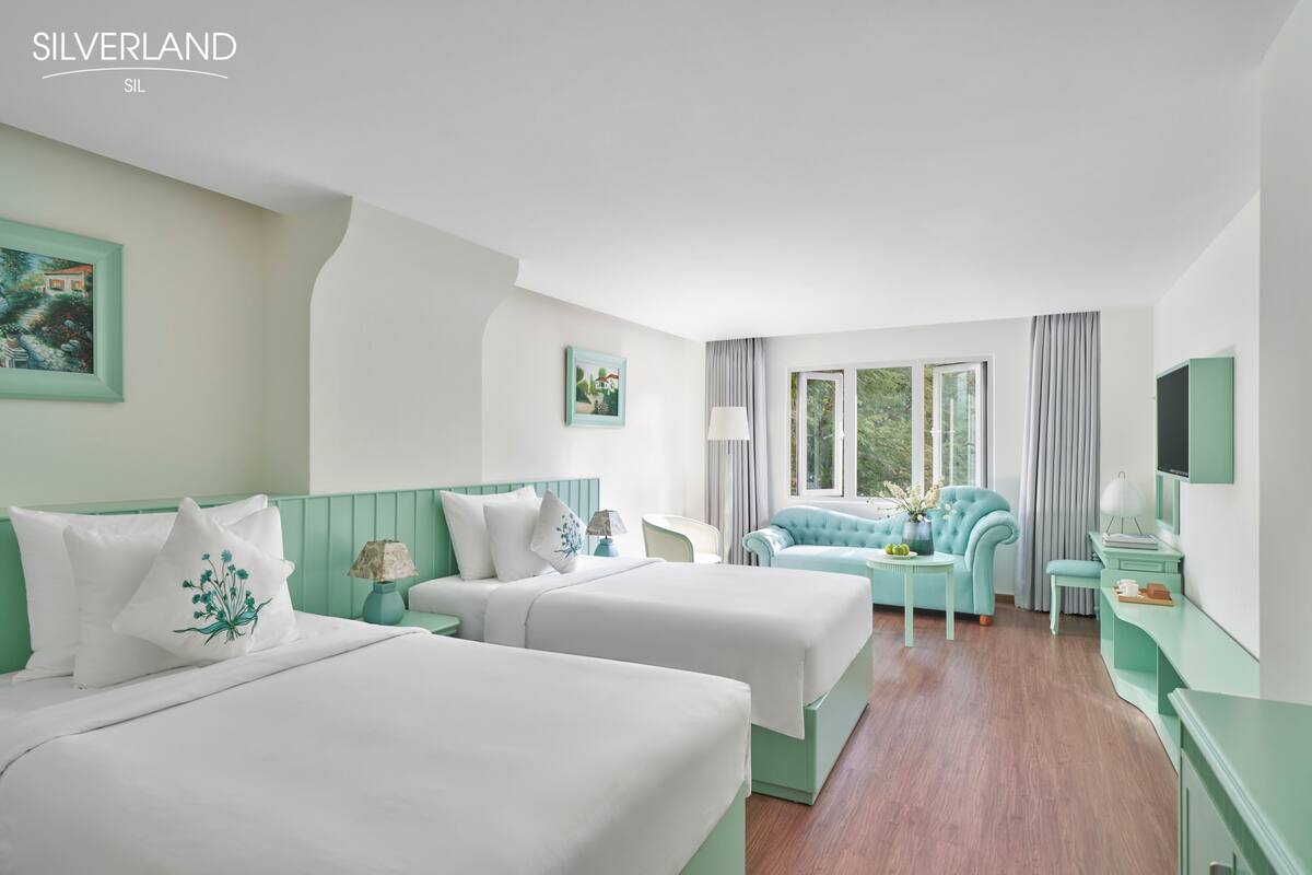 Una habitación de hotel con dos camas, un sofá, una mesita y un televisor.