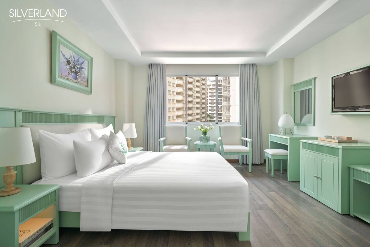 Habitación de hotel con una cama grande, un escritorio, una silla, un televisor y una ventana con vistas a la ciudad.