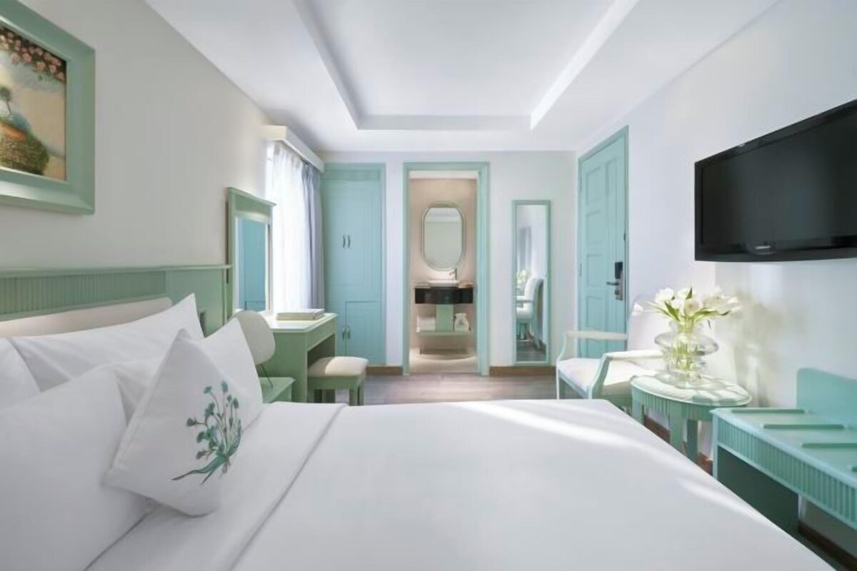 Habitación de hotel con cama, escritorio, silla, televisión y baño visible a través de una puerta abierta.