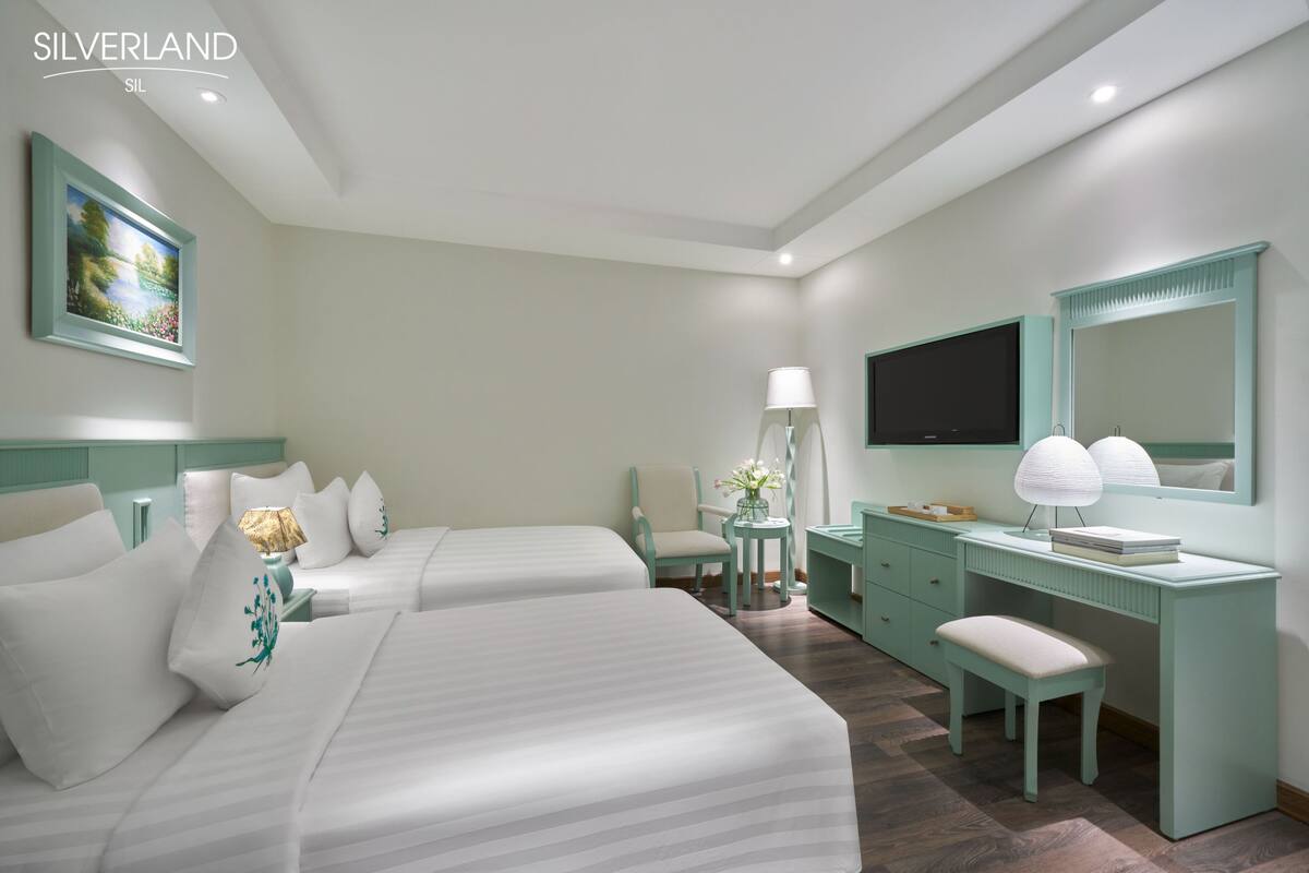 Habitación de hotel con dos camas, un escritorio, una silla, un televisor y un espejo.