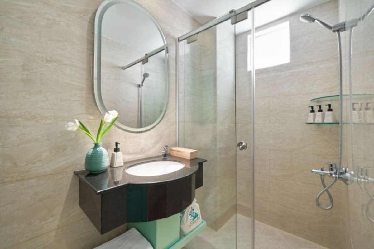 Een moderne badkamer met een glazen douchecabine, een ronde spiegel en een in het aanrecht geïntegreerde wasbak met een bloevas.