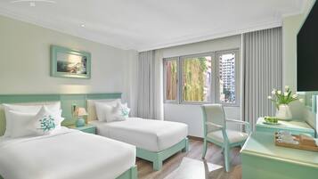 Una habitación de hotel con dos camas, una silla, un escritorio con una bandeja y una ventana con cortinas.