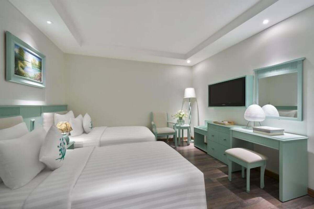Una habitación de hotel con dos camas, un escritorio, una silla, un televisor y un espejo.