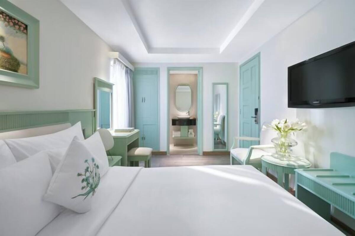 Habitación de hotel con cama, escritorio, silla, televisión y baño visible a través de una puerta abierta.