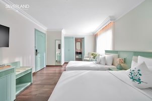 A hotel room with two beds, a TV, a desk, and a bathroom visible through an open door.