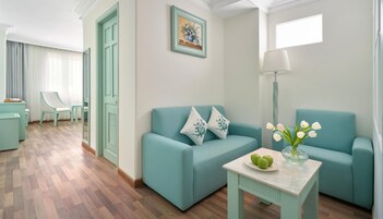 A modern living room with teal sofas, a small table with apples and a vase of flowers, and a painting on the wall.