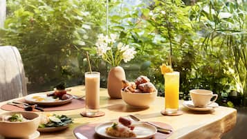 Et spisebord dækket med forskellige retter, et højt glas appelsinjuice og en vase med blomster.