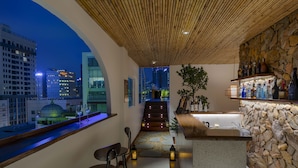 Un área de bar moderna con pared de piedra, taburetes y vista a la ciudad.