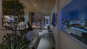 Un pasillo estrecho con una zona de bar en un lado, un espacio de estar con taburetes y un amplio ventanal que ofrece vistas de la ciudad.