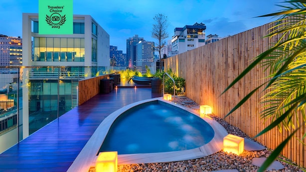 Un área de piscina en la azotea con cubierta de madera, piscina pequeña y plantas aledañas.