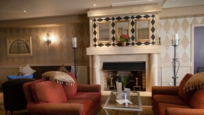 A living room with two red sofas, a glass coffee table, a fireplace with a diamond-patterned mantle, and wall-mounted sconces. - Brook Mollington Banastre Hotel and Spa (Chester)