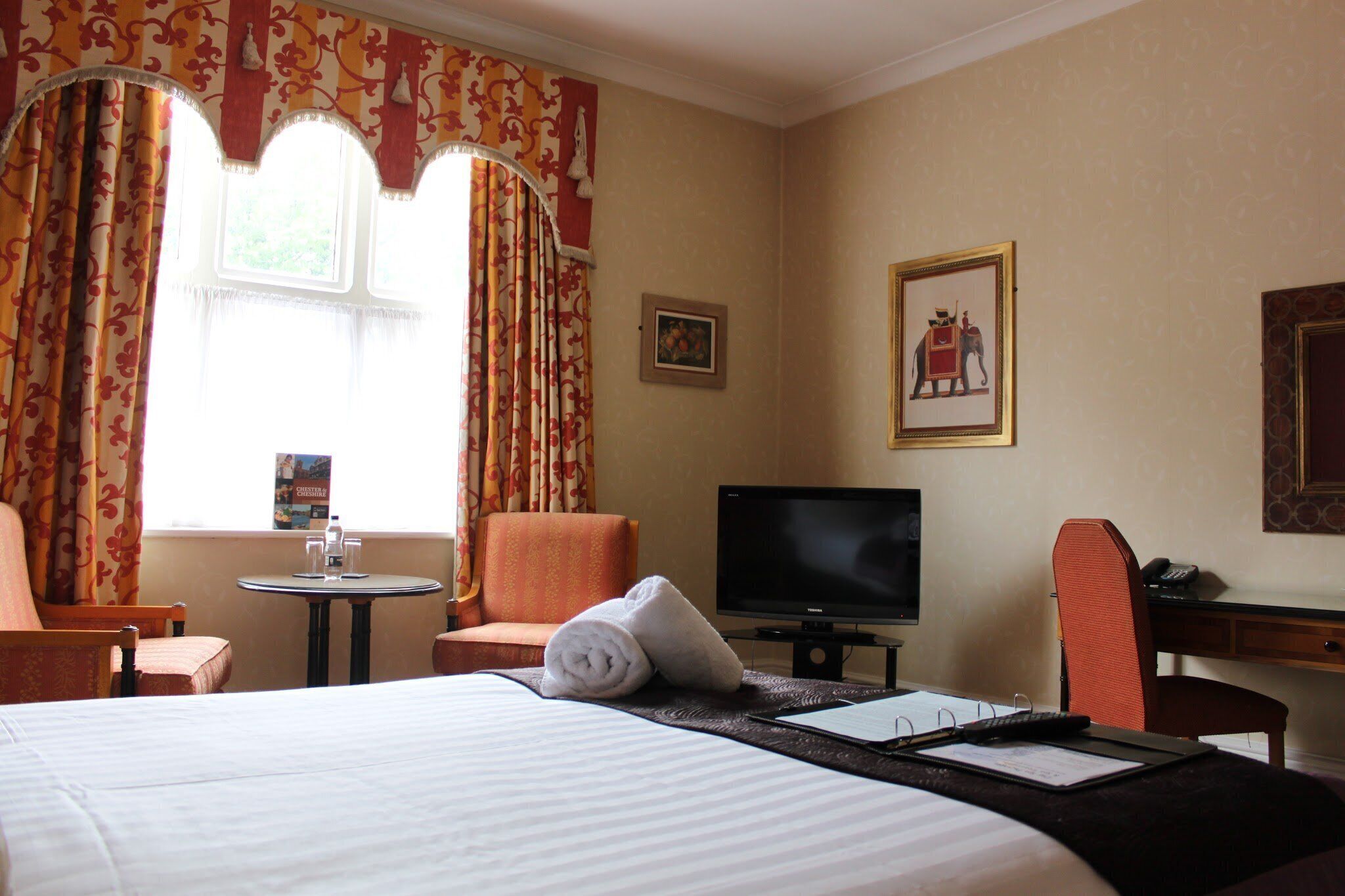 A hotel room with a bed, a desk, a television, a chair, and a window with curtains.