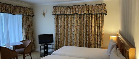 A hotel room with two beds, a TV, a small table with chairs, and curtains.