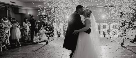 Una ceremonia de boda con confeti cayendo, invitados con atuendo formal y una novia y un novio abrazándose.