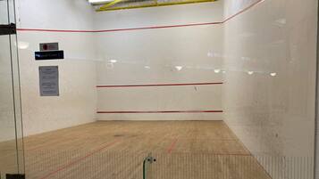 A squash court with clear lines, a wooden floor, and a glass door.