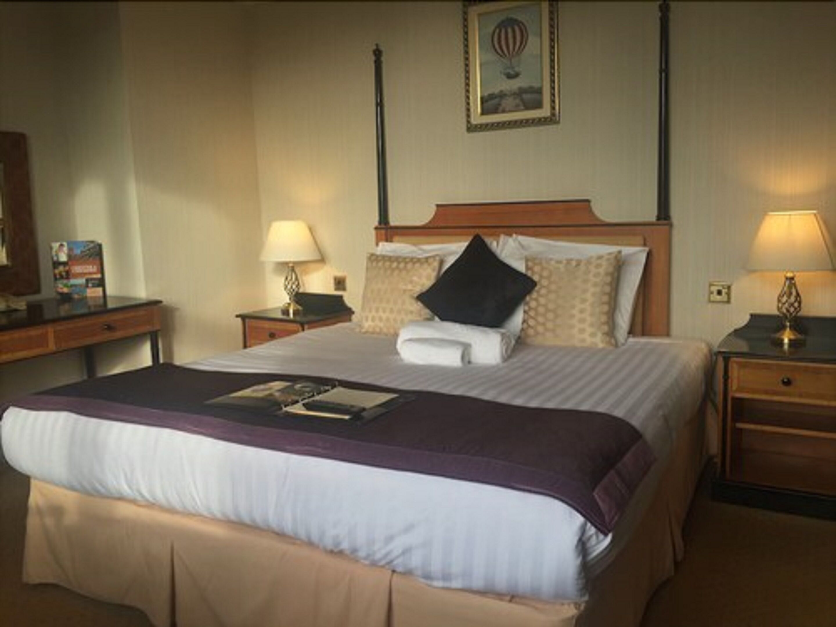 A hotel room with a large bed, two bedside tables with lamps, a wooden headboard, and a framed picture on the wall.