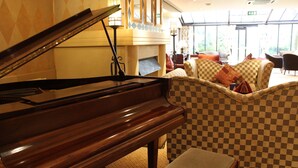 A grand piano in a well-lit room with checkered armchairs and a fireplace. - Brook Mollington Banastre Hotel and Spa (Chester)