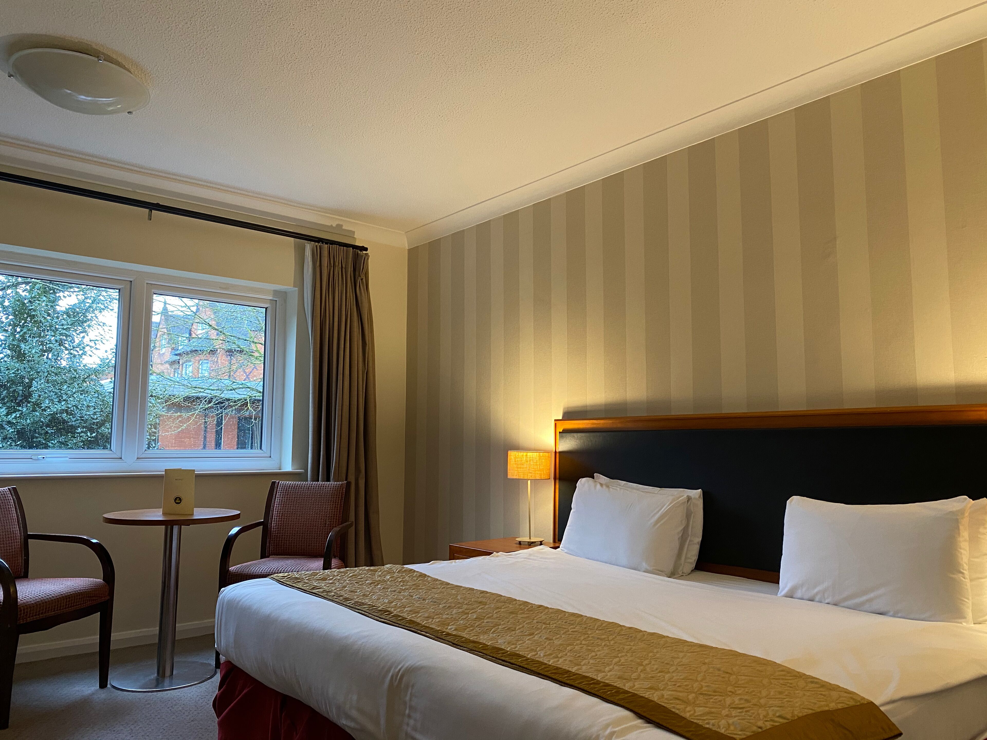 Une chambre d’hôtel avec un grand lit, une petite table, une chaise et une fenêtre avec des rideaux.
