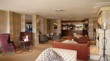 A hotel lobby with a checkered sofa, striped armchairs, a bar area, and a fireplace.