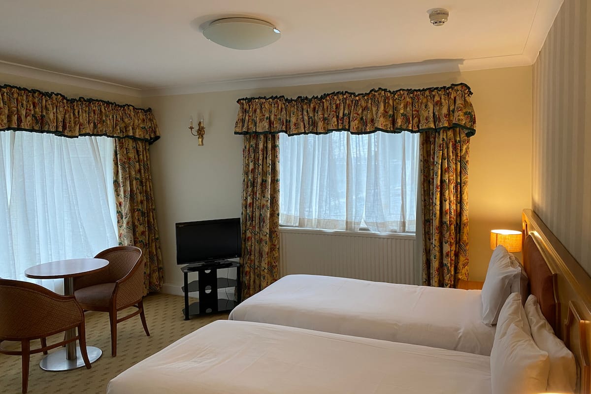 A hotel room with two beds, a TV, a small table with chairs, and curtains.