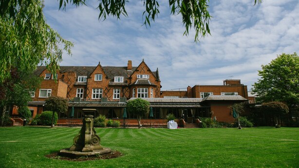 A large brick building with a symmetrical facade, multiple windows, and a well-maintained lawn with a stone fountain. - Brook Mollington Banastre Hotel and Spa (Chester)
