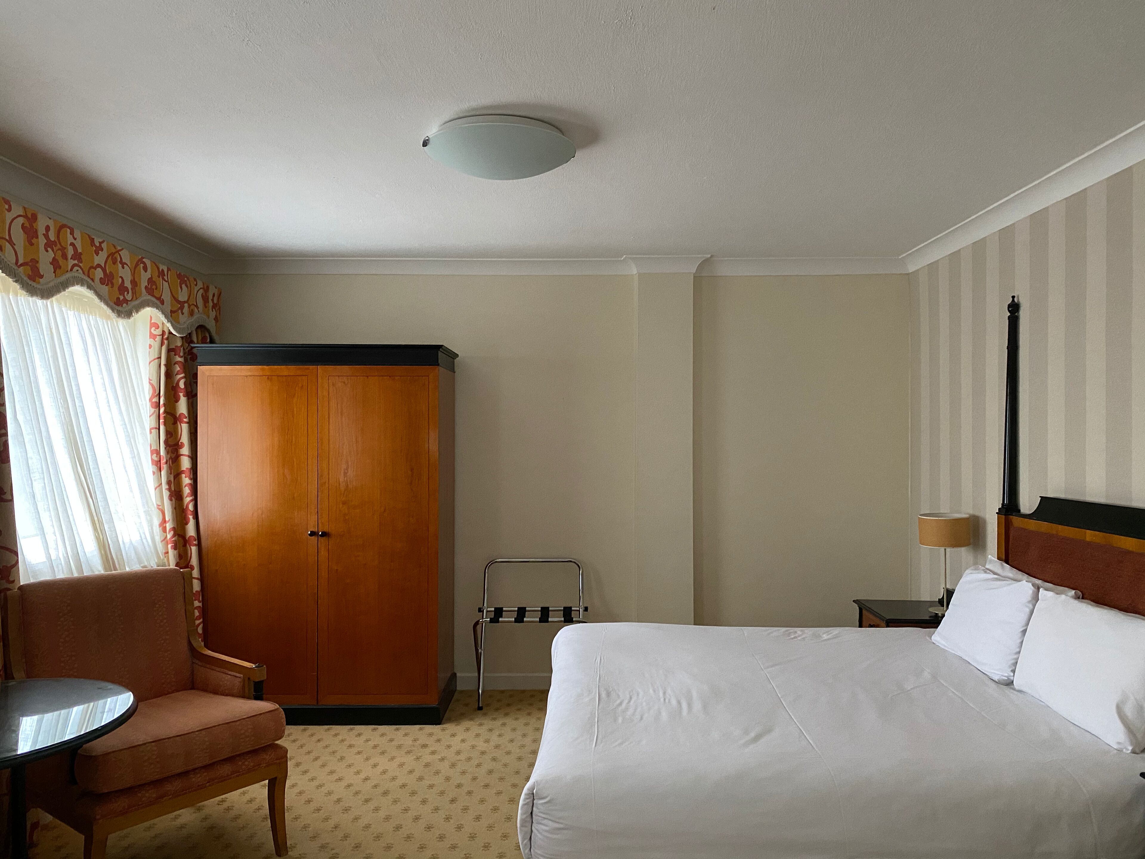 Ein Hotelzimmer mit Bett, Stuhl, Kleiderschrank, Schreibtisch und Lampe.