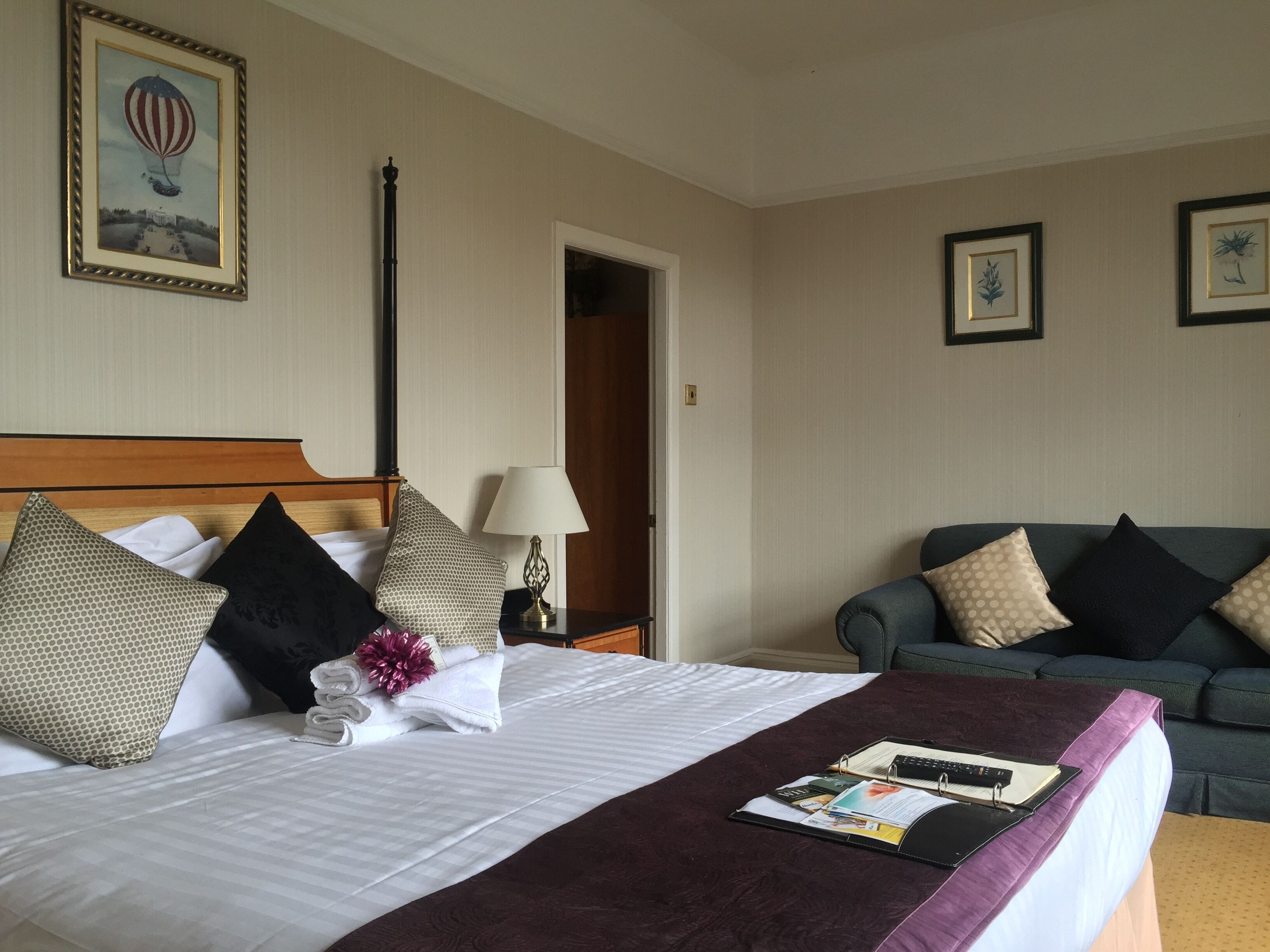 Une chambre d’hôtel avec un lit bien fait, une table de chevet avec une lampe, un canapé et un tableau encadré au mur.