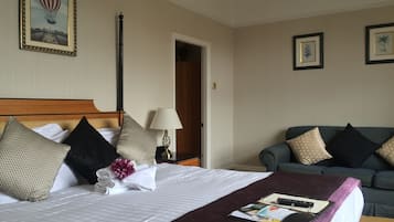 Quarto de hotel com cama bem arrumada, mesa de cabeceira com abajur, sofá e quadro na parede.