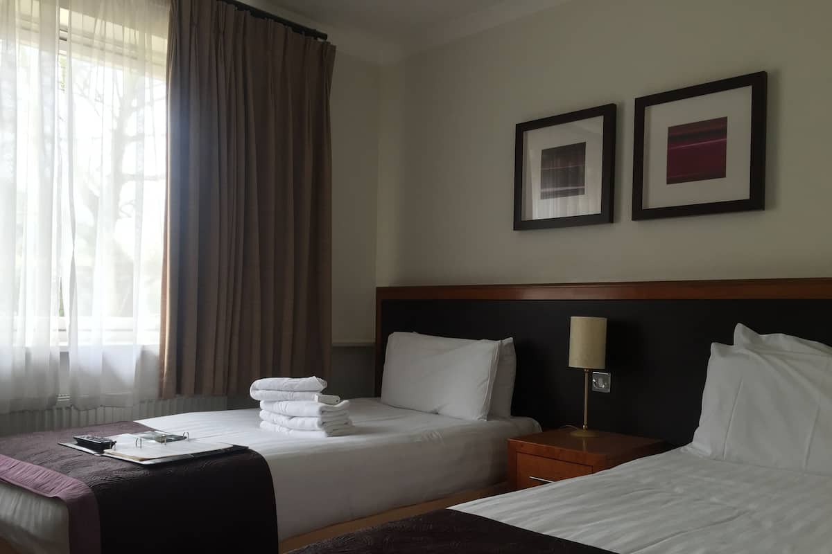 A hotel room with two beds, a nightstand, a lamp, and two framed pictures on the wall.