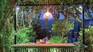 An outdoor dining area with a wooden table and green metal chairs, surrounded by lush greenery and a view of distant mountains. - Koukounaria Hotel & Suites (Zakynthos)