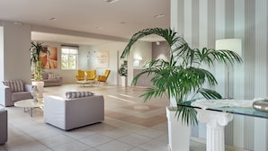 A spacious living room with a large potted plant, a sofa, and a coffee table. - Koukounaria Hotel & Suites (Zakynthos)