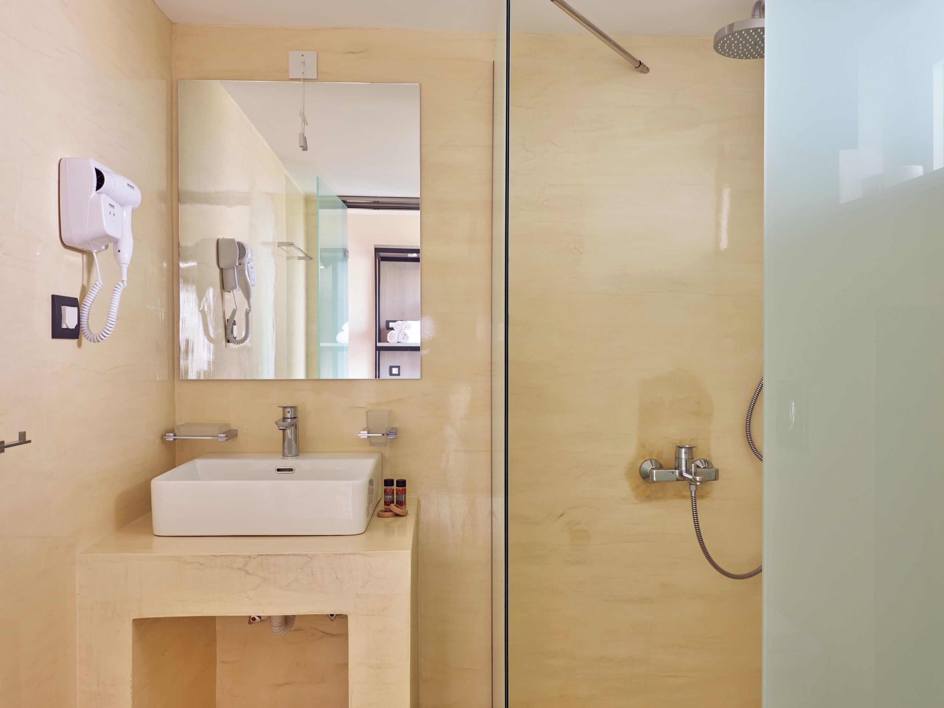 A bathroom with a glass shower enclosure, a sink with a mirror above it, and a hairdryer mounted on the wall.