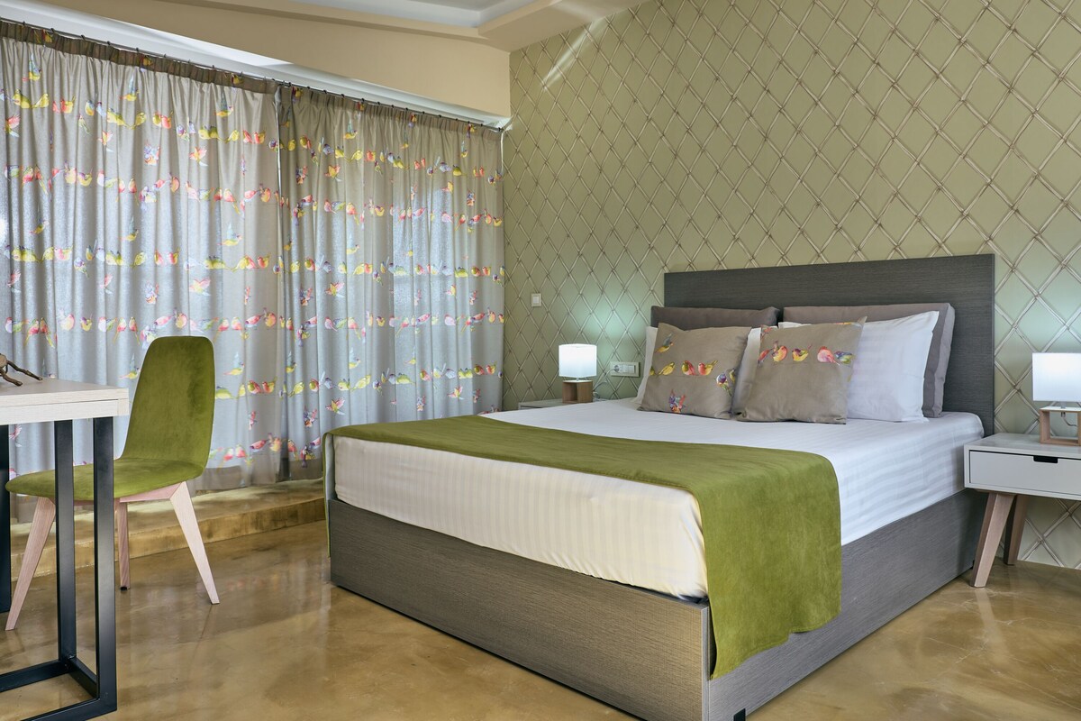 A hotel room with a bed, a desk, a chair, and a nightstand with a lamp.