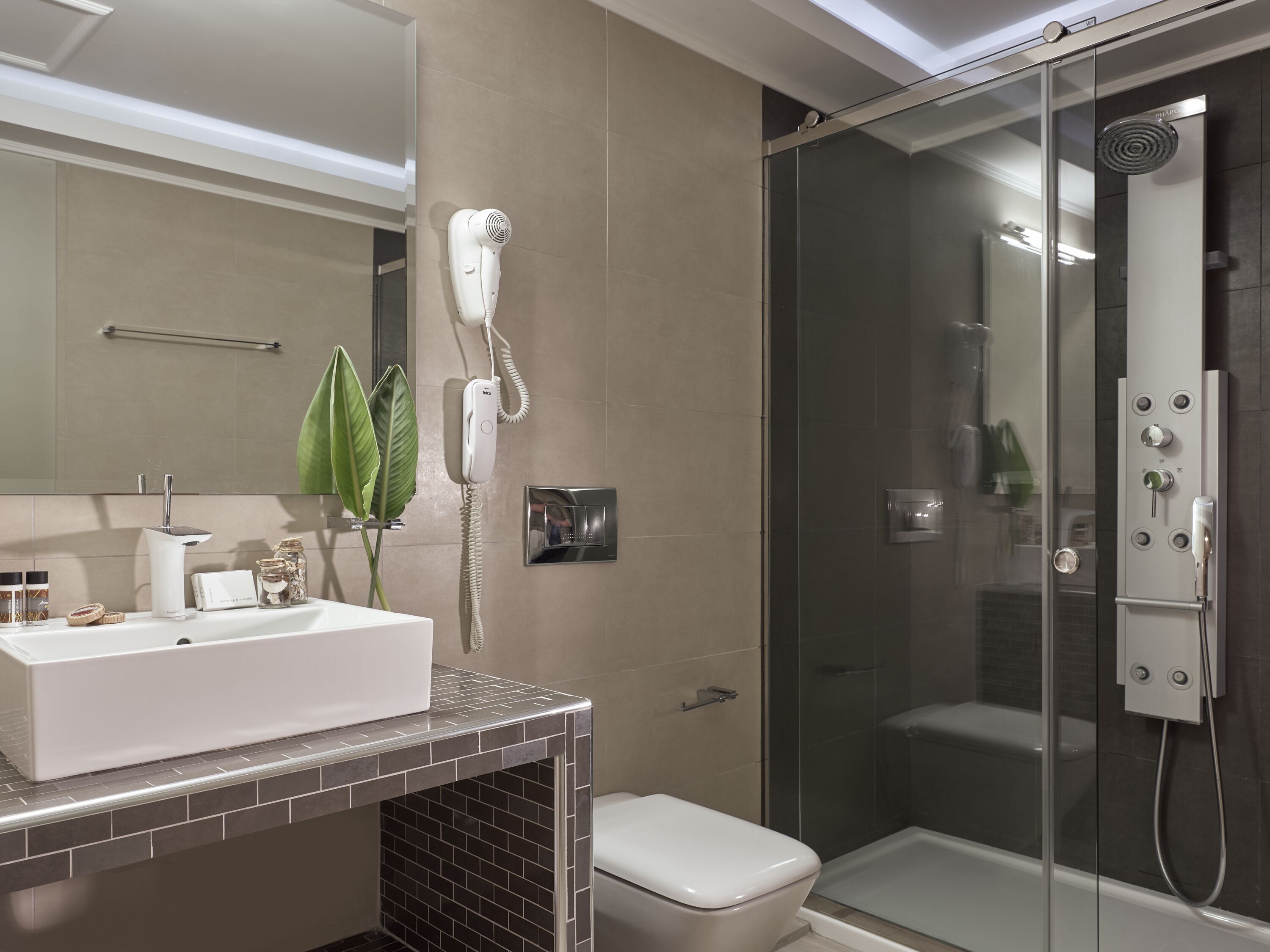 A modern bathroom with a white sink, a hairdryer mounted on the wall, a glass-enclosed shower, and a toilet.