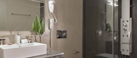 A modern bathroom with a white sink, a hairdryer mounted on the wall, a glass-enclosed shower, and a toilet.