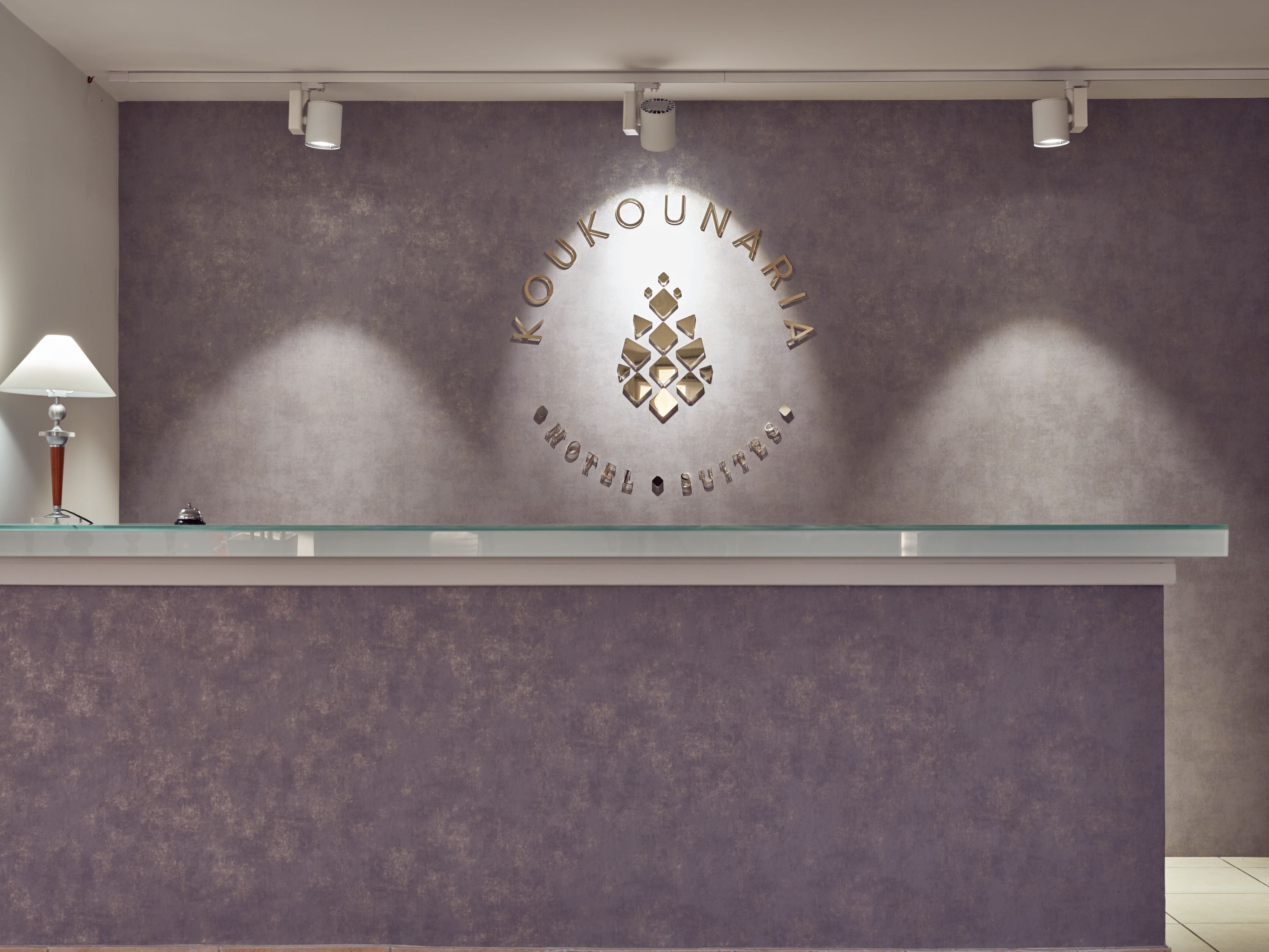 A reception desk with a glass top and a wall-mounted sign displaying the hotel name and logo.