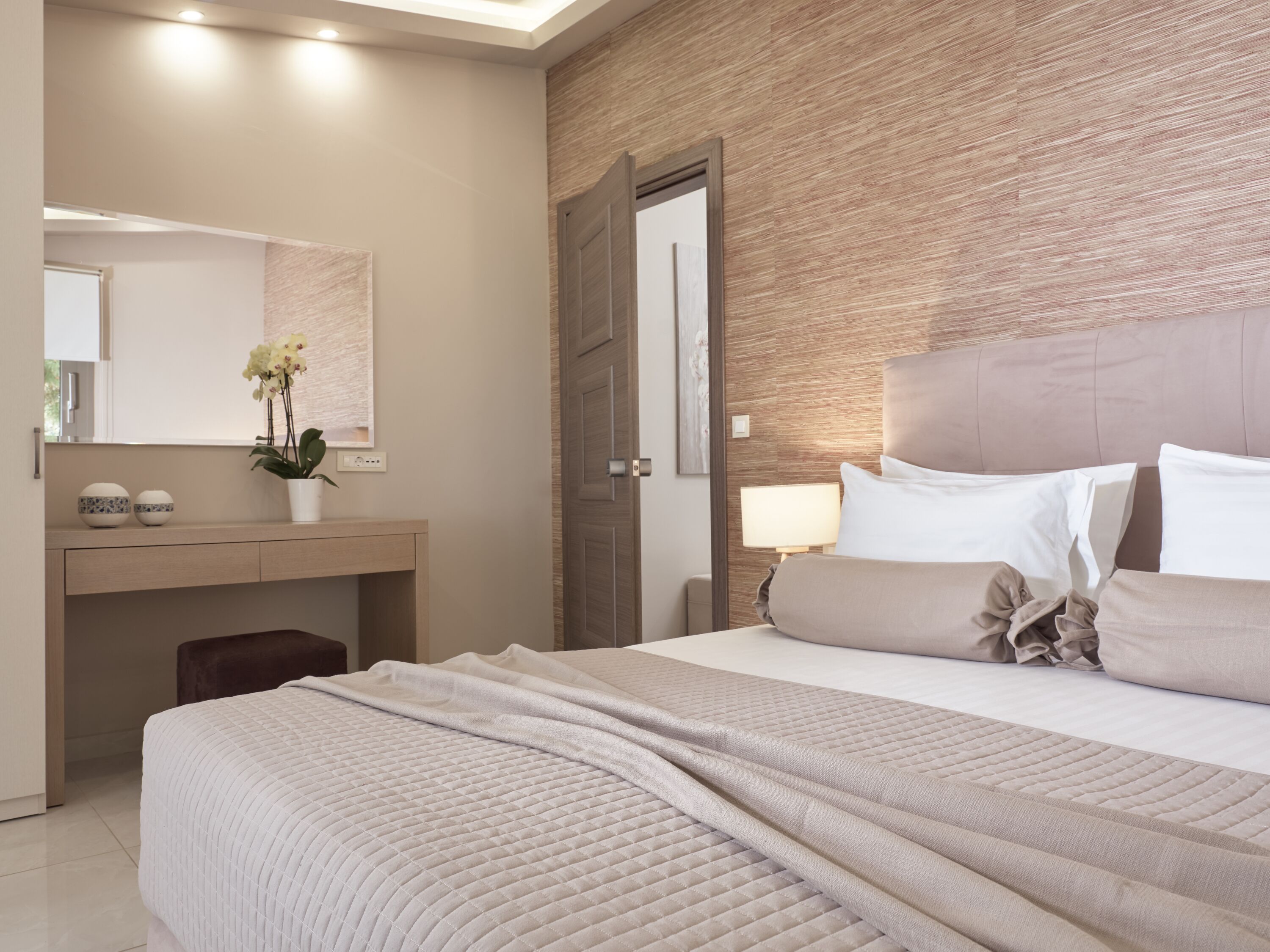 A modern bedroom with a large bed, a bedside table, a mirror, and a wooden accent wall.